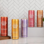 Five cans of 'Good Idea' sparkling water on a white surface with a gray tiled wall background.