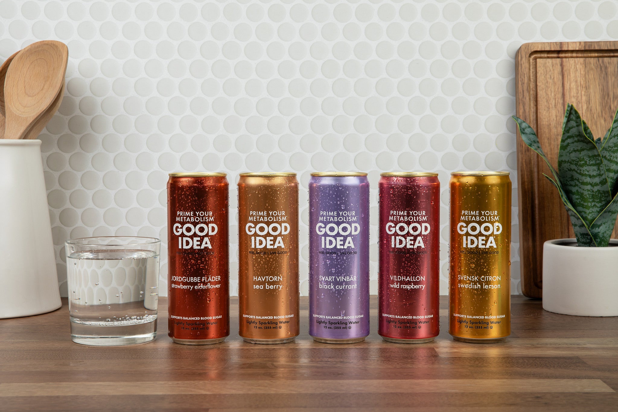 All five flavors of Good Idea sparkling water with a glass filled with sparkling water on the side