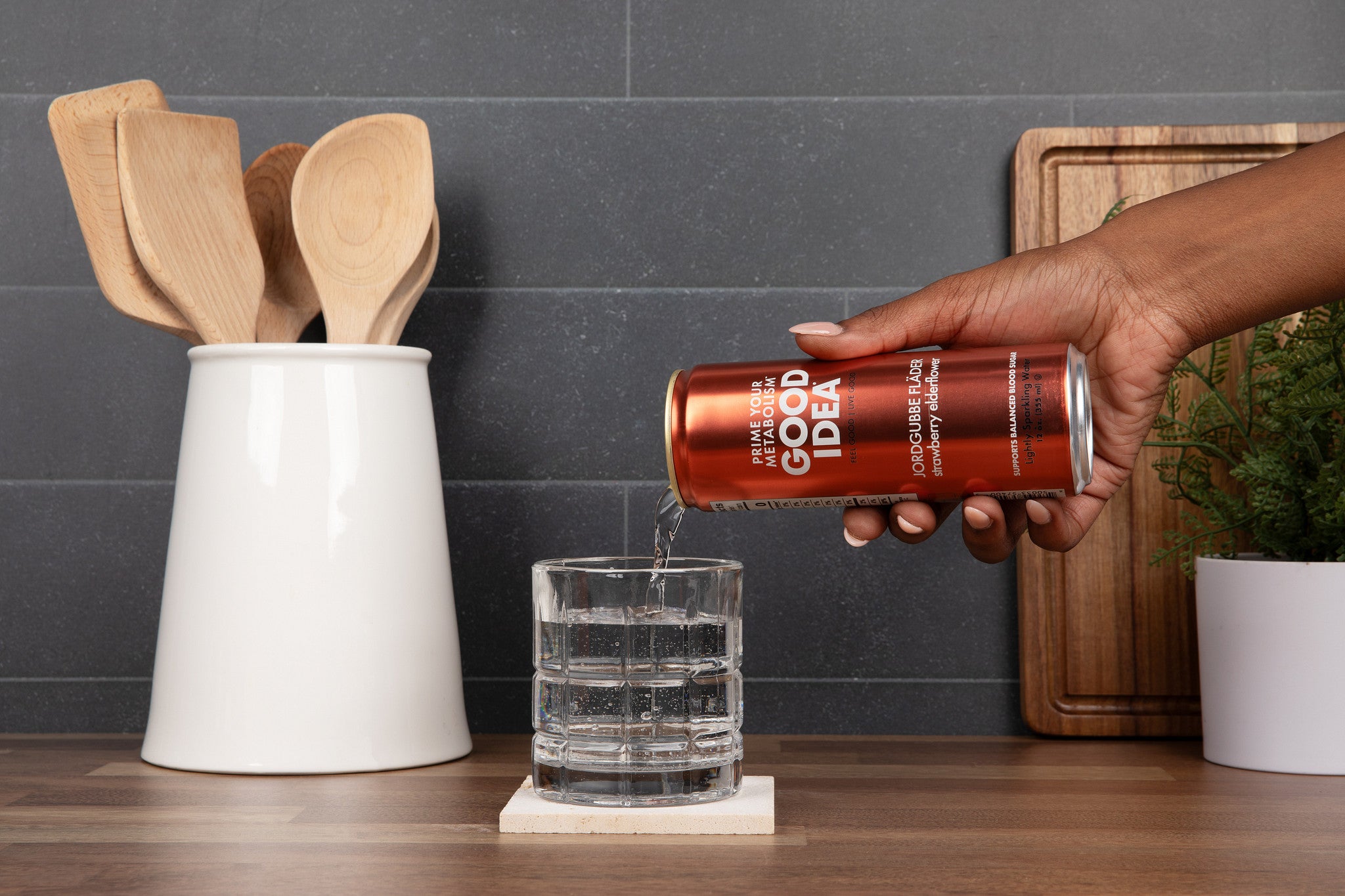 Person pouring a can of Good Idea sparkling water into a glass on a kitchen counter