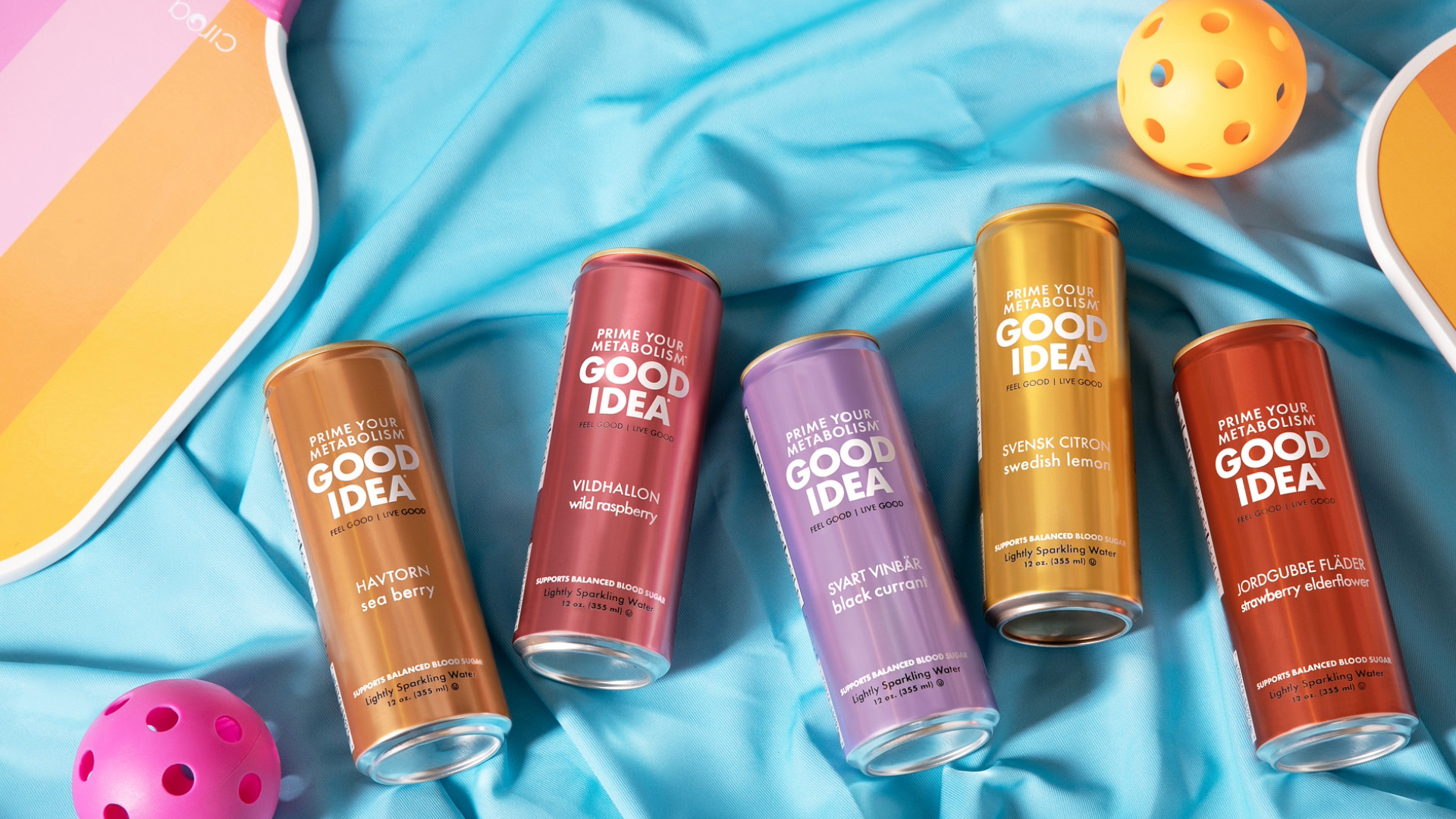 Five cans of GOOD IDEA on a blue fabric background with a colorful pickleball theme