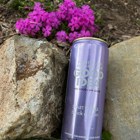 Can of GOOD IDEA Black Currant with rocks and pink flowers in the background